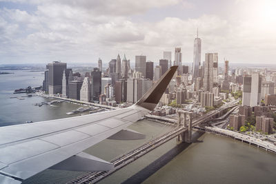 Cropped image of airplane wing flying over river by sea