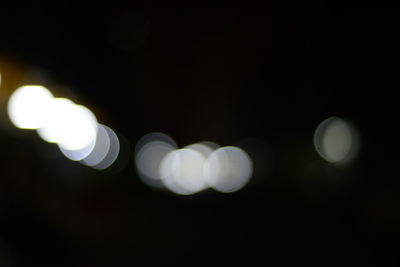 Defocused image of illuminated light bulb against sky at night