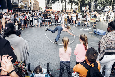 Audience looking at street performer on footpath in city