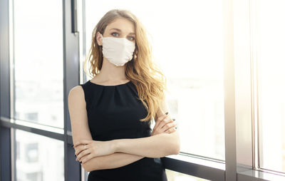 Portrait of a young woman standing against window