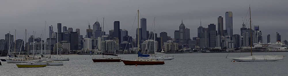 Sailboats moored on sea by buildings against sky in city