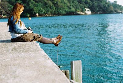 Side view of woman sitting on pier by lake