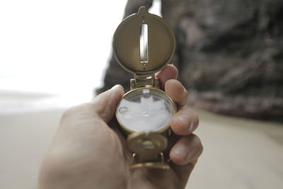 Close-up of hand holding compass at beach against rock formations