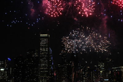 Firework display in city against sky at night