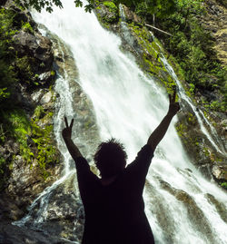 Rear view of woman standing against waterfall