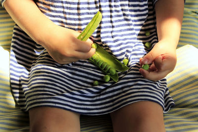 Midsection of girl holding green peas while sitting on bed at home