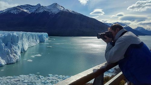 Man photographing iceberg against sky