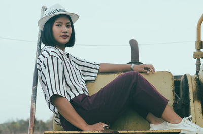 Portrait of smiling teenage girl in hat sitting against sky