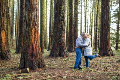Retired couple kiss romantically in forest.