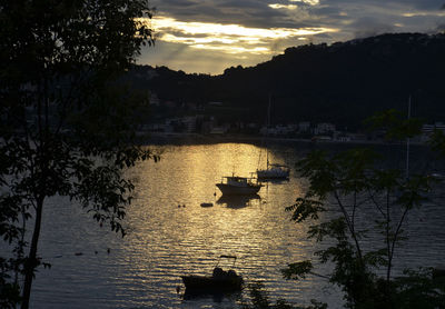 Silhouette boat in river against sky at sunset