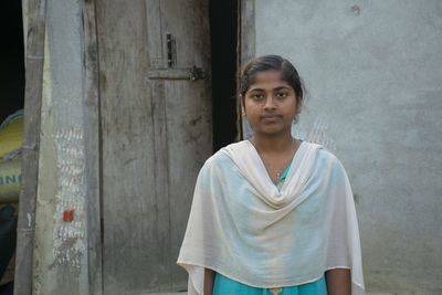 Portrait of smiling teenage girl standing against door of the house