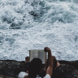 Rear view of man holding book on rock against sea
