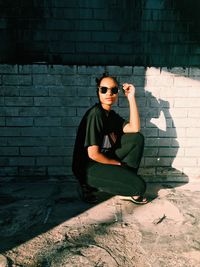 Side view portrait of woman crouching by wall on sunny day