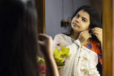 A beautiful indian woman in white saree wearing silver earrings in front of mirror with smiling face