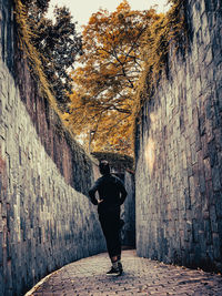 Rear view of woman standing on footpath against wall