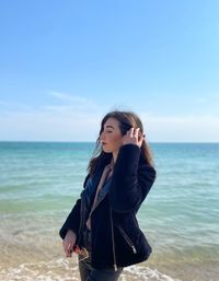 Young woman standing at beach against sky