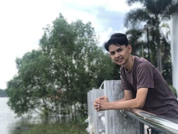 Portrait of smiling young man sitting against trees