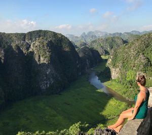 Woman sitting on retaining wall while looking at mountains