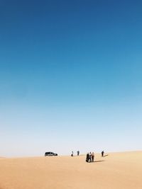 People on desert against clear blue sky