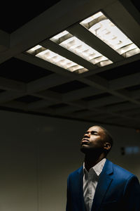African businessman with eyes closed standing under illuminated fluorescent light in subway
