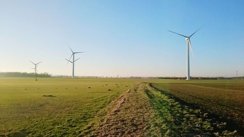 Windmills on landscape against clear sky during sunset