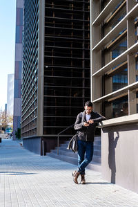 Man using smartphone outdoors, standing next to office building