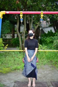 Full length of woman wearing mask sitting on swing at park