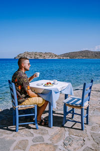 Side view of man sitting on chair at beach