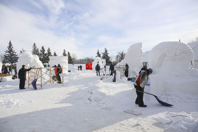 People on snow covered field against sky