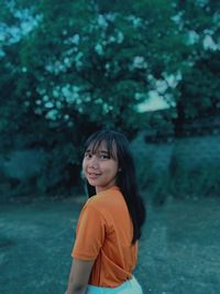 Portrait of a smiling young woman standing against trees