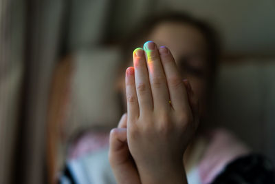 Close up of a girl's hand with rainbow coloured light reflected on fingers