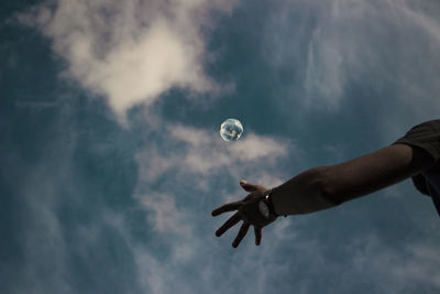 Low angle view of cropped hand catching crystal ball against black background