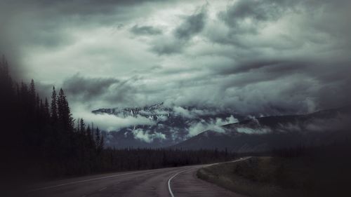 Road by trees against storm clouds