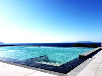 Swimming pool by sea against clear blue sky