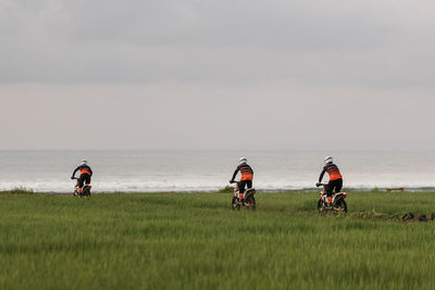 People riding motorcycle on field against sky