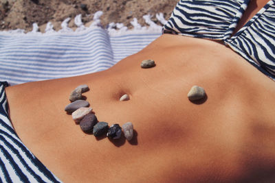 Midsection of woman with pebbles on stomach at beach