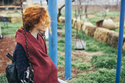 Redhead woman sitting on swing at playground