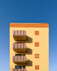 Low angle view of yellow building against clear blue sky