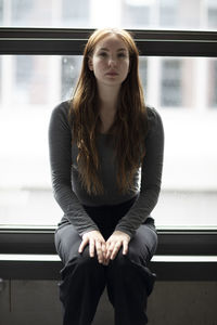 Portrait of young woman sitting on railing against window