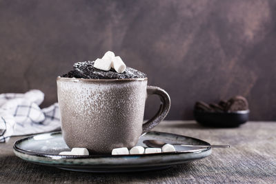 Chocolate cake in a mug with marshmallows and powdered sugar on the table for homemade dessert