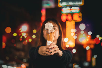 Portrait of woman holding ice cream cone at night