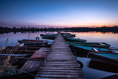 Boats moored at lake against sky during sunset