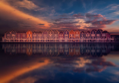 Reflection of building in sea against orange sky