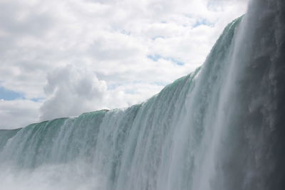 Low angle view of waterfall against cloudy sky