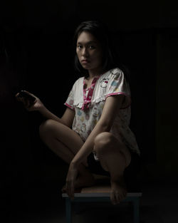 Young woman looking away while sitting against black background