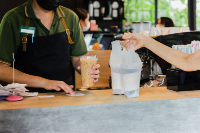Barista wearing face mask serving coffee in plastic bag to take out in cafe