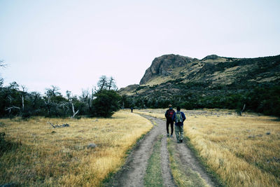 Rear view of people walking on footpath against sky in autumn