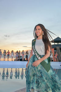 Young woman standing against wall with sky in background