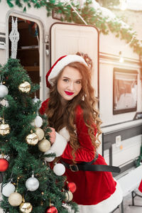 Portrait of smiling young woman holding christmas tree at home