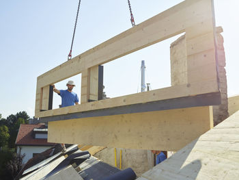 Workers installing wooden frame on top of house with crane machine